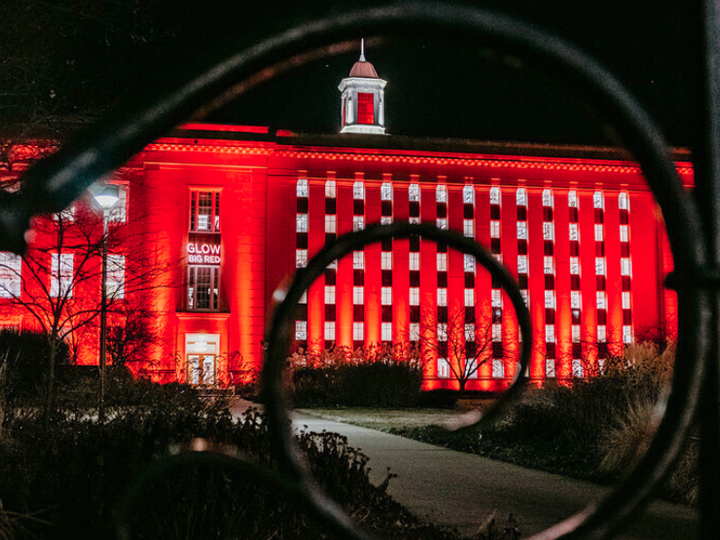 Image of Love Library South as seen from R Street, with the exterior lit up with red lights